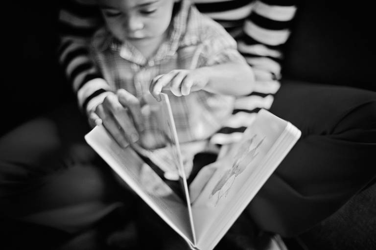 Little boy reading book on mom’s lap
