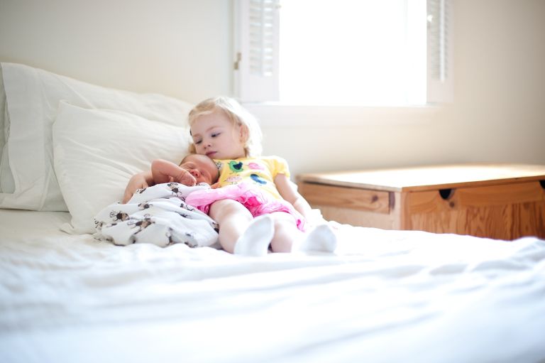 Little sister snuggling baby brother on bed